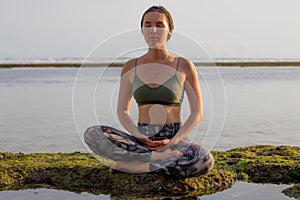 Young woman sitting on the rock in lotus pose, meditating, practicing yoga and pranayama. Deep breath and concentration with