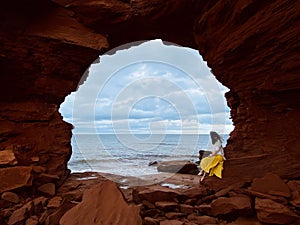 Young woman sitting on rocks under the sea cliffs at Cavendish Beach, Prince Edward Island, Canada