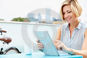 Young Woman Sitting On Roof Terrace Using Digital Tablet