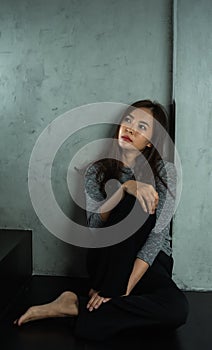 Young woman sitting sad at wall, depression emotion, looking above space in dark room, Portrait of young beautiful woman or female