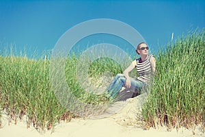 Young woman sitting in sand dunes amongst tall grass in Luskentyre, Isle of Harris, Scotland