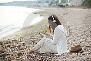 Young woman sitting on a sea sand and listening music by earphones, calm and meditative