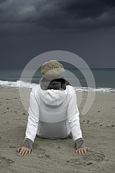 Young woman sitting by the sea with stormy sky, looks at the horizon thoughtfully