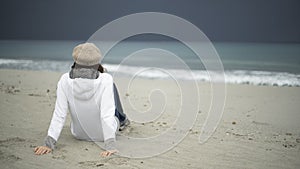 Young woman sitting by the sea with stormy sky, looks at the horizon thoughtfully