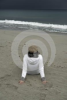 Young woman sitting by the sea with stormy sky, looks at the horizon thoughtfully