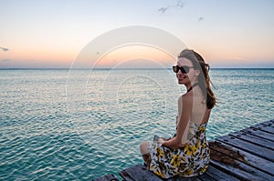 Young woman sitting on seaside jetty at sunset