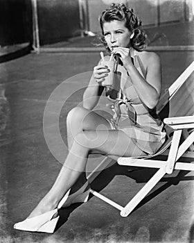 Young woman sitting on sling chair, sipping a drink photo