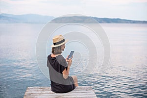 Young woman sitting with smart phone on a beach. Relaxation, freelance, travel lifestyle, connection concept