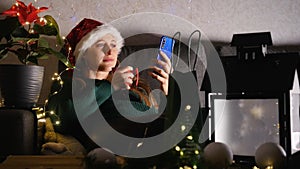 Young woman sitting on the sofa in Christmas decorated living room using mobile phone.