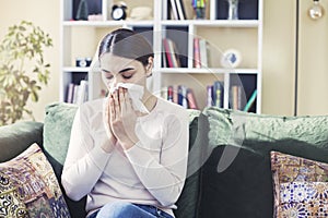 Young woman sitting on sofa covered  freezing blowing running nose got fever caught cold sneezing in tissue, sick girl having infl