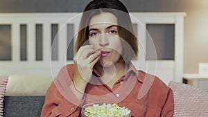 Young woman sitting on the sofa, eating popcorn and watching TV