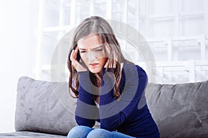 Young Woman Sitting On Sofa having headache migraine