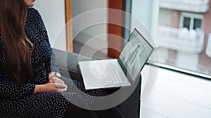 Young woman sitting on sofa at home having conversation with virtual therapist on laptop