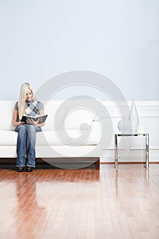 Young Woman Sitting on Sofa Reading Book