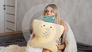 Young woman sitting on sofa and thinking. Beautiful girl holding cushion