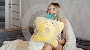 Young woman sitting on sofa and thinking. Beautiful girl holding cushion