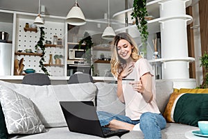 Young woman sitting on the sofa using laptop computer and credit card for online shopping and ordering groceries and food for home