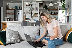 Young woman sitting on the sofa using laptop computer and credit card for online shopping and ordering groceries and food for home