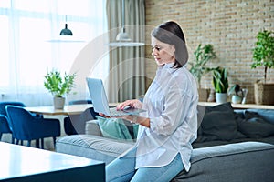 Young woman sitting on sofa using laptop for work, freelancing, learning