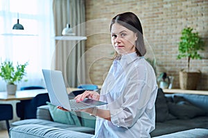 Young woman sitting on sofa using laptop for work, freelancing, learning