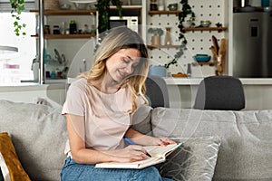 Young woman sitting on the sofa writing down the guest list of her friends whom she will invite to her bachelorette party for her