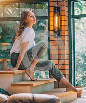 Young woman sitting on a stairs and posing. Cosy room in big house, interior design. Beauty model girl