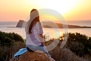 Young woman sitting on the stone enjoying peaceful moment of sunset