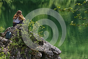Young woman sitting on a stone on the shore of the lake Superior Fusine lake, Julian Alps, Italy, Europe. photo