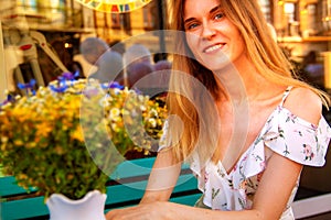 Young woman sitting at street cafe near flowers and green plants. Concept of cozy place in open air and resting.