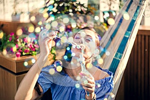 A young woman is sitting in a summer outdoor cafe in hammock and blowing soap bubbles