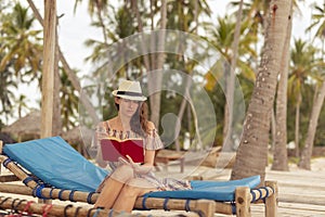 Woman sitting on sun bed on tropical beach, reading a book