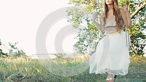 Young woman sitting and swaying on rope swing on oak tree. Female mood, romance, lonely girl misses in summer, concept leisure