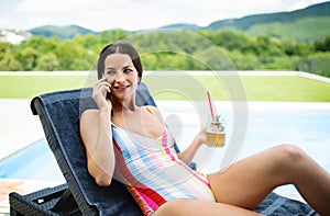 Young woman sitting by swimming pool outdoors in backyard garden, relaxing.