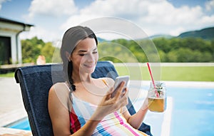 Young woman sitting by swimming pool outdoors in backyard garden, relaxing.