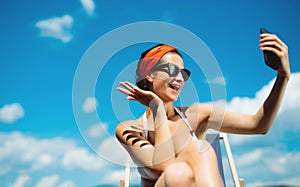 Young woman sitting by swimming pool outdoors in backyard garden, taking selfie.