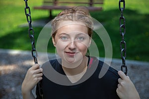 young woman sitting in a swing at the park playing outside happy enjoyment leisure