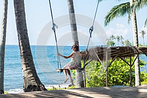 young woman sitting on the swing on the tropical beach, paradise island Bali, Indonesia. Sunny day, happy vacation
