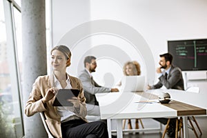 Young woman sitting by the table with digital tablet in modern office in front of her team