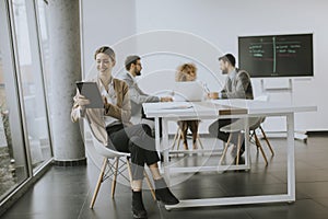 Young woman sitting by the table with digital tablet in modern office in front of her team