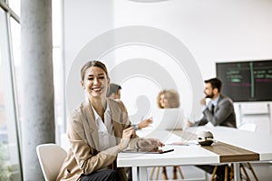 Young woman sitting by the table with digital tablet and paper chart in modern office in front of her team