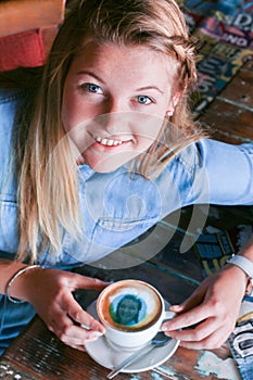 Young woman sitting at a table holding a coffee cup with her face printed on the foam.