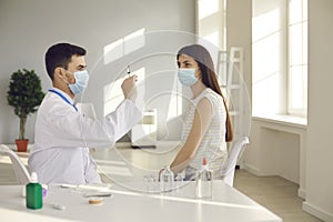 Young woman sitting at table at the hospital and waiting for doctor to get syringe ready