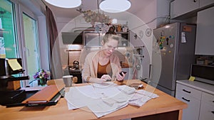 Young woman sitting at the table in kitchen and calculating bills. Home accounts department. Checking the bills.