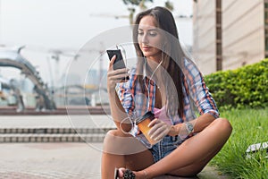 Young woman sitting at a table outdoors using her mobile phone. Female reading text messages on smartphone in the park.