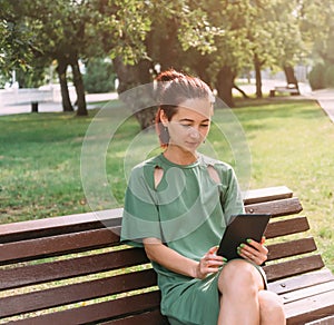 Young woman sitting with tablet in summer park.