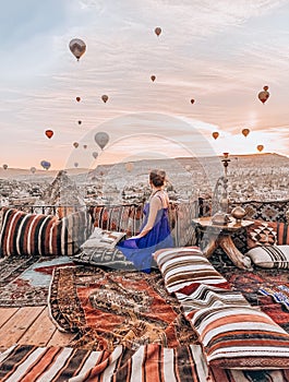Young woman sitting on the terrace in Cappadocia watching sunrise and air balloons
