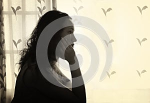 Young woman sitting and thinking near bright window light. black and white filtered image