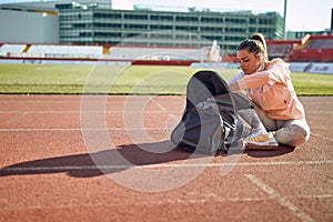 A young woman is sitting on the track and preparing for a training at the stadium. Sport, athletics, athletes