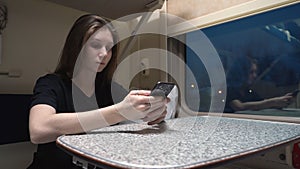 Young woman is sitting in a train carriage. She uses the phone and looks out the train window. Concept of travel