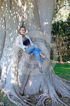 Young woman sitting on a trunk of a huge tree in Kurnell area, Australia. She is happy and smiling photo